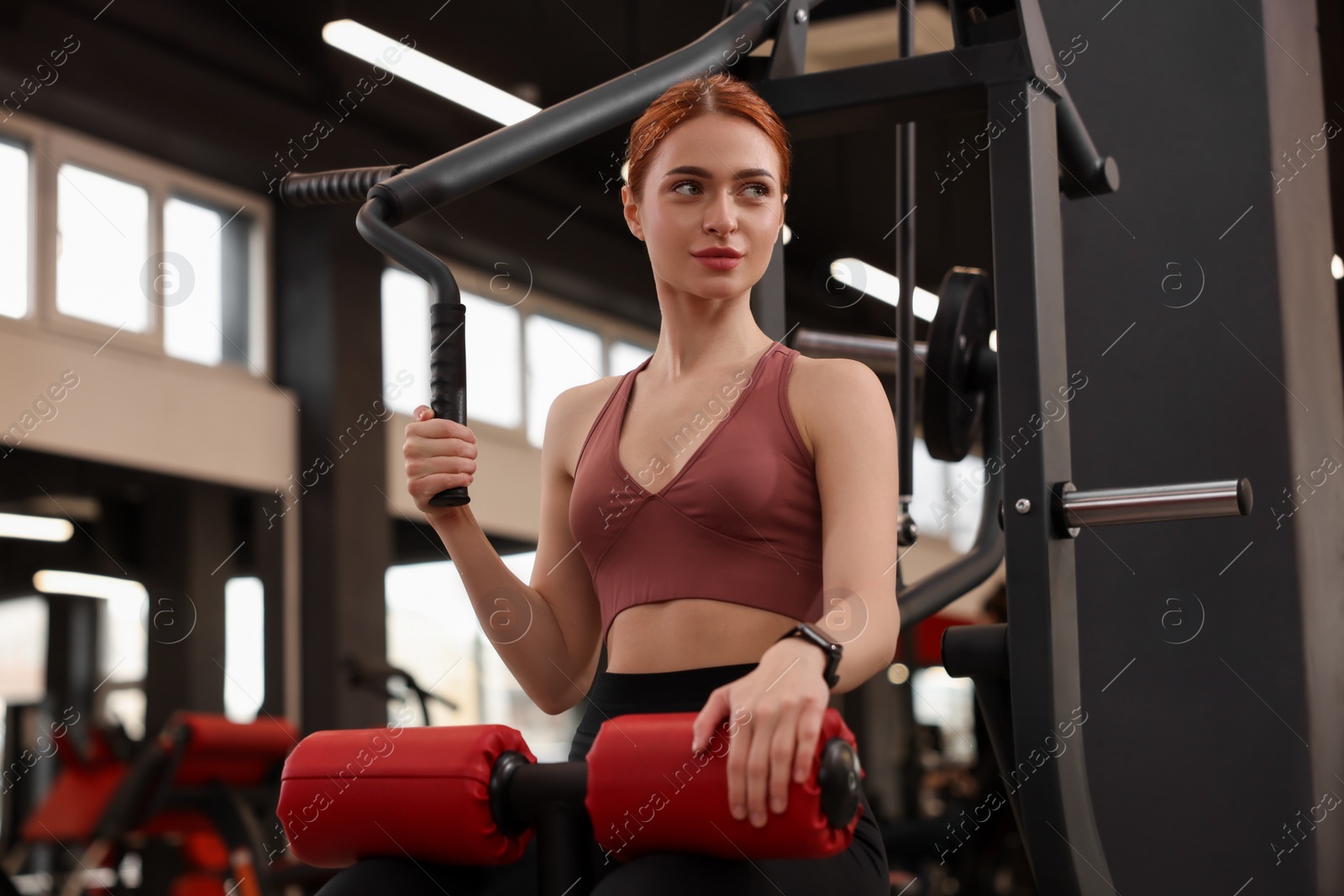 Photo of Athletic young woman training with lat pulldown machine in gym