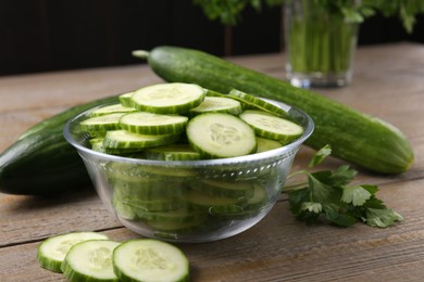 Photo of Cut cucumber in glass bowl, fresh vegetables and parsley on wooden table, closeup