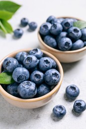 Photo of Tasty fresh blueberries in bowls on light grey table, closeup