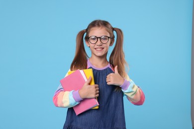 Happy schoolgirl with books showing thumbs up on light blue background
