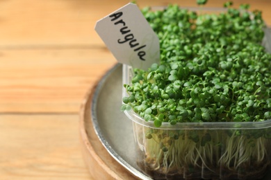 Photo of Sprouted arugula seeds in plastic container on wooden table, closeup