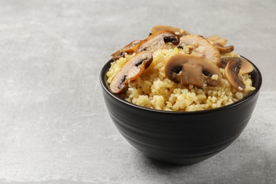 Photo of Delicious bulgur with mushrooms in bowl on gray table, closeup. Space for text