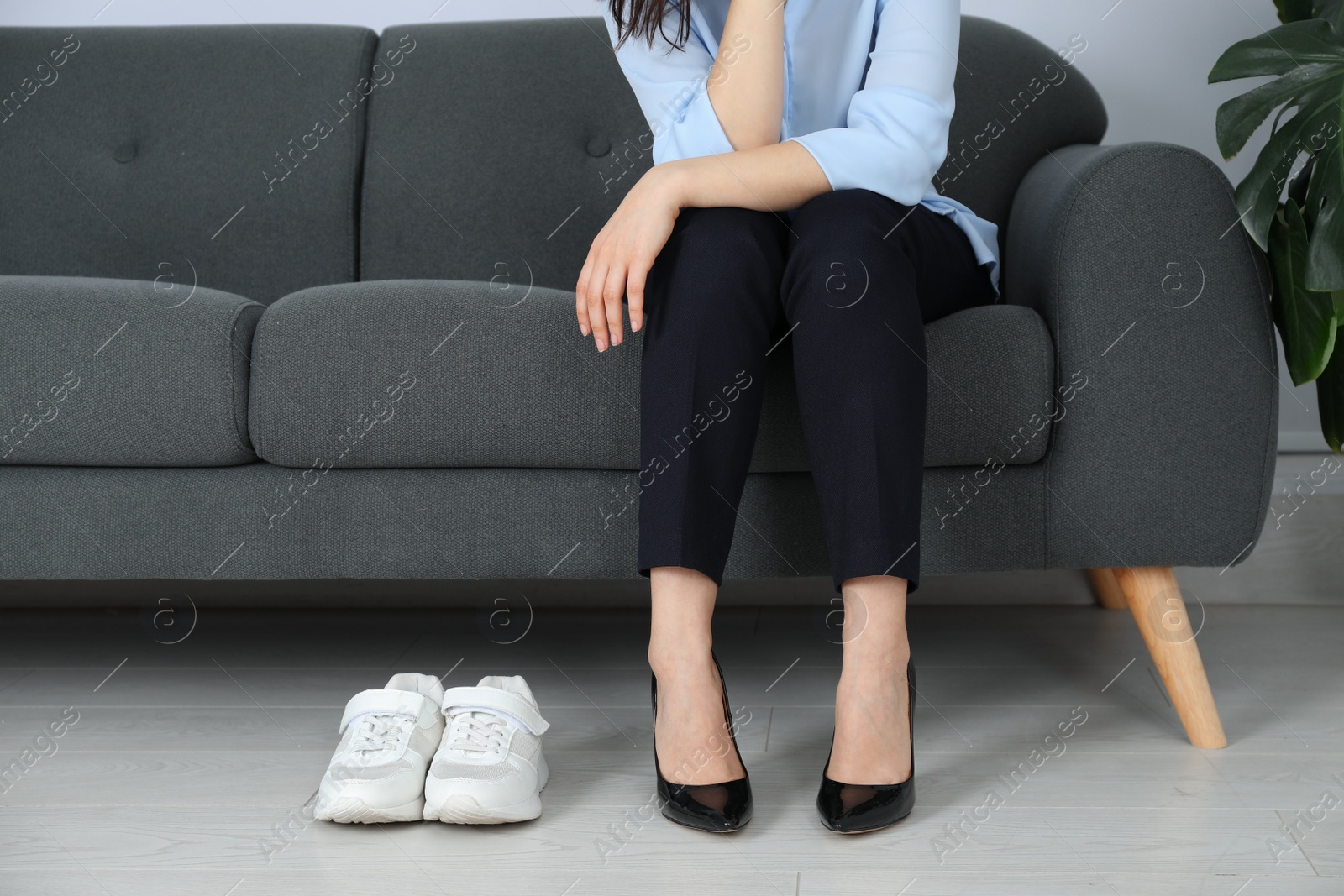 Photo of Comfortable sneakers near businesswoman wearing high heel shoes indoors, closeup