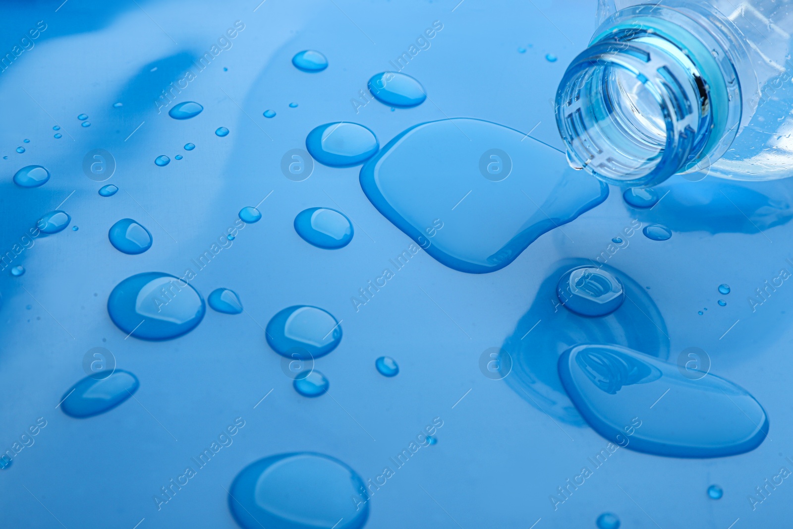 Photo of Drops of spilled water and plastic bottle on blue background, closeup