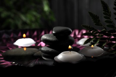 Burning candles and spa stones in bowl with water, closeup