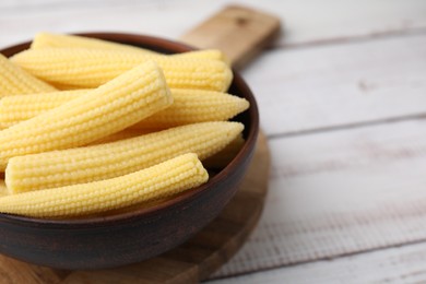 Photo of Tasty fresh yellow baby corns in bowl on white wooden table, closeup. Space for text