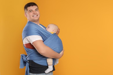 Father holding his child in sling (baby carrier) on orange background. Space for text