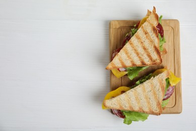 Photo of Wooden board with tasty sandwiches on white table, top view. Space for text