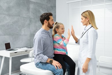 Photo of Happy father and daughter having appointment with doctor. Pediatrician and patient giving high five in clinic