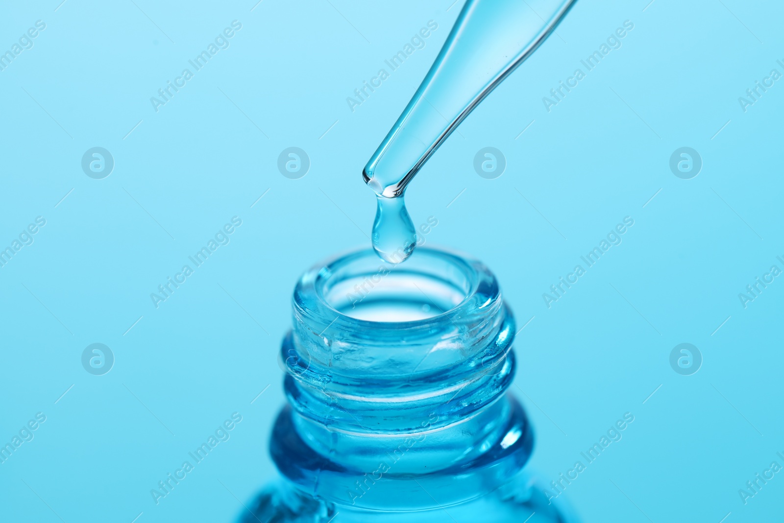 Photo of Dripping liquid from pipette into glass bottle on light blue background, closeup