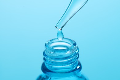 Dripping liquid from pipette into glass bottle on light blue background, closeup