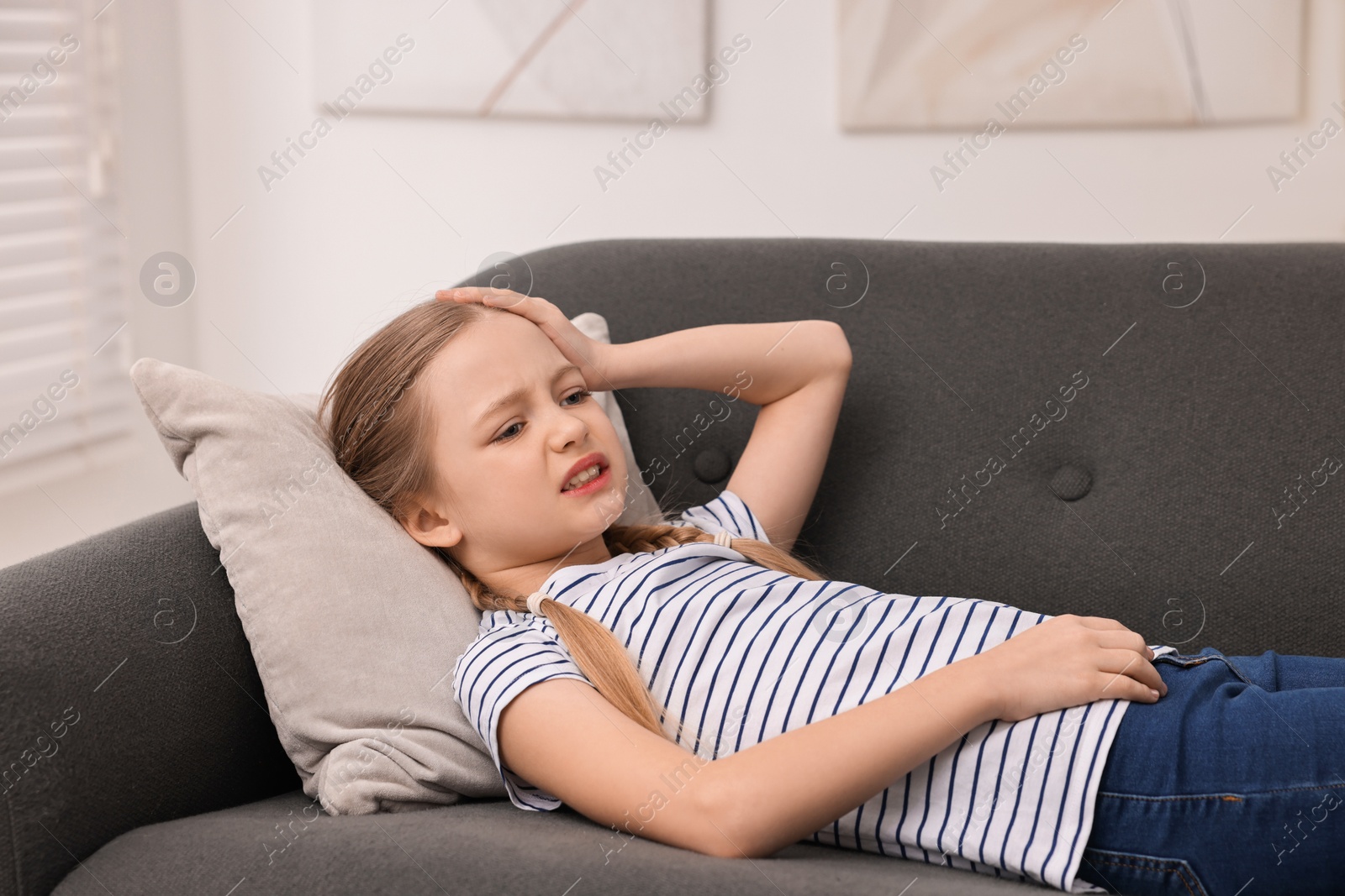 Photo of Little girl suffering from headache on sofa indoors