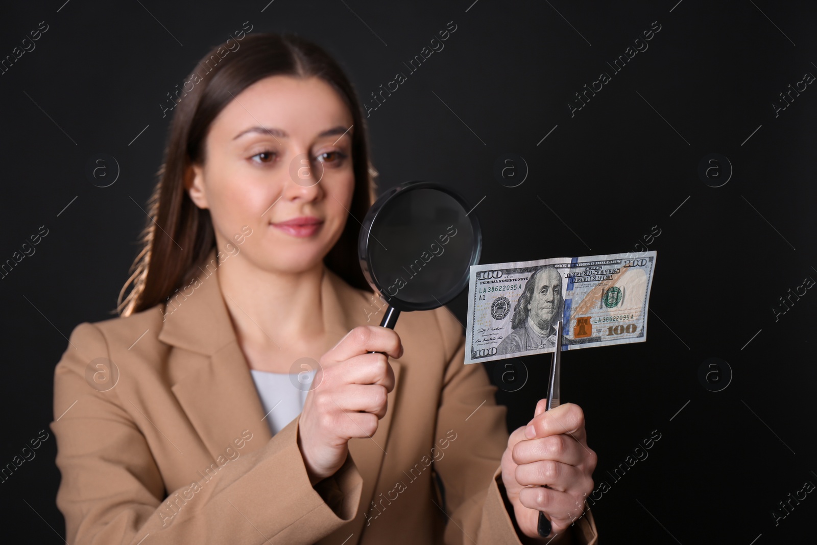Photo of Expert authenticating 100 dollar banknote with magnifying glass against black background, focus on hand. Fake money concept
