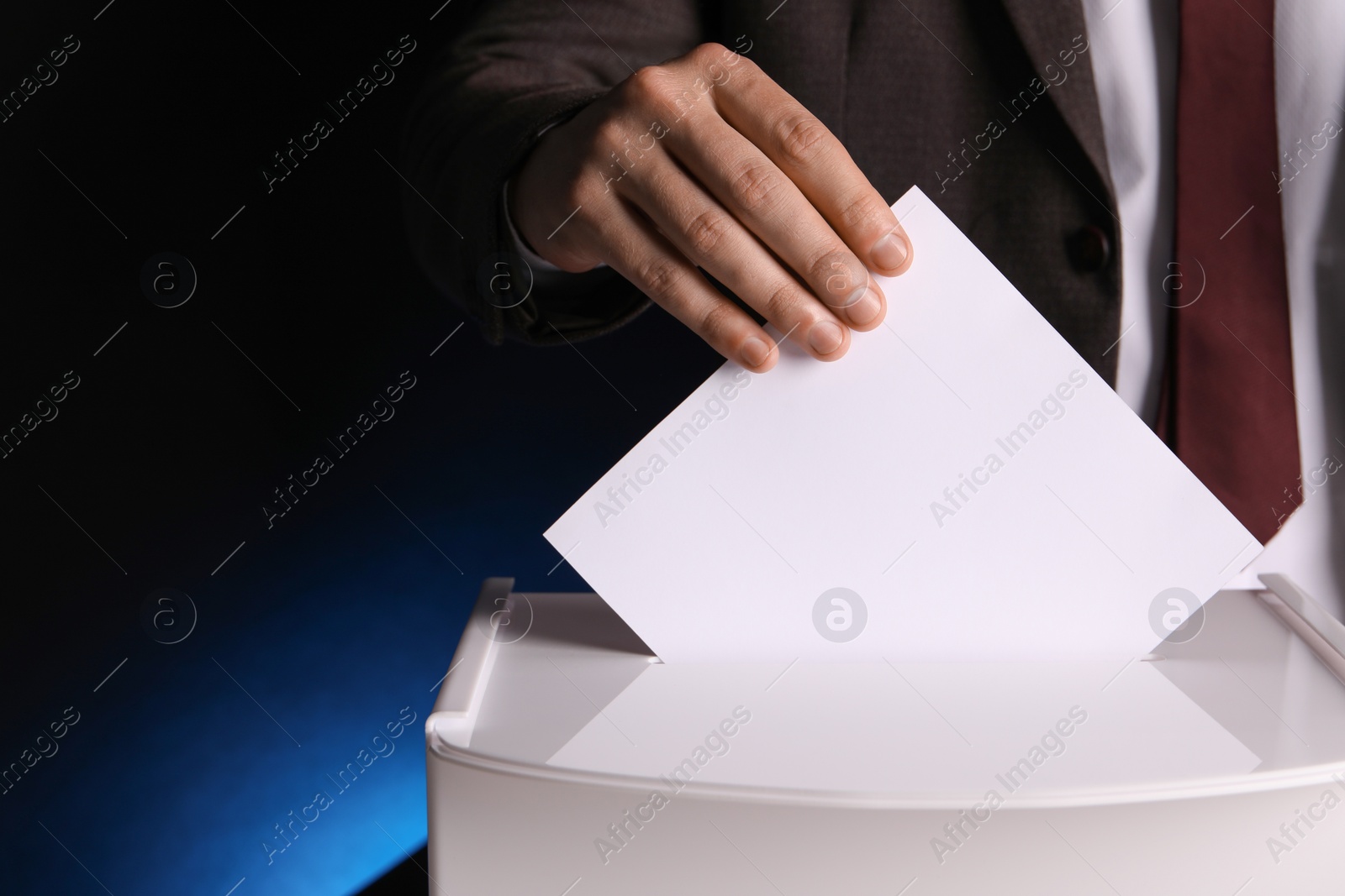 Photo of Man putting his vote into ballot box on dark blue background, closeup. Space for text