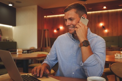 Photo of Happy man talking on smartphone in cafe