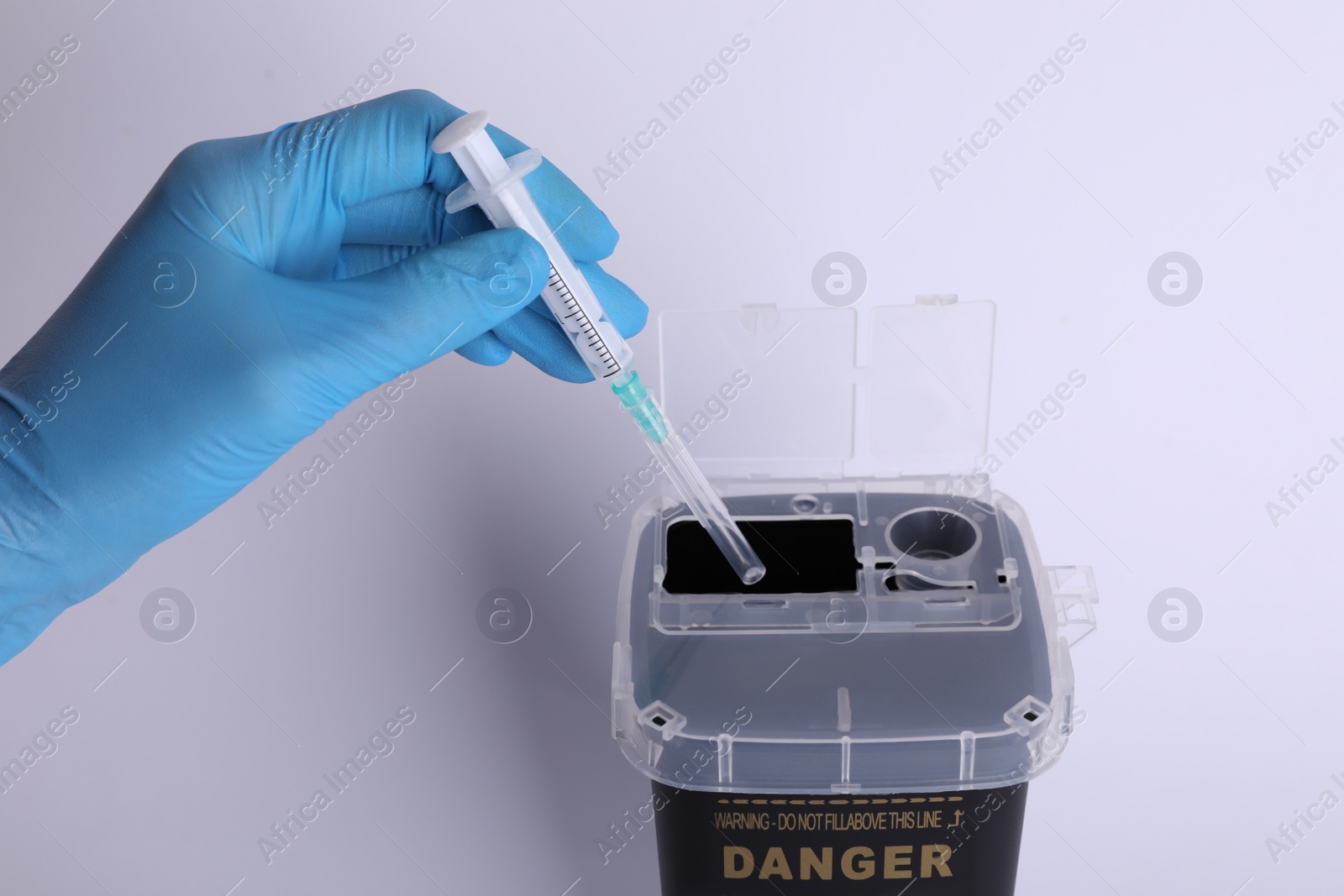 Photo of Doctor throwing used syringe into sharps container on white background, closeup