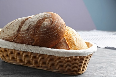 Loaves of tasty fresh bread in wicker basket on grey table, closeup