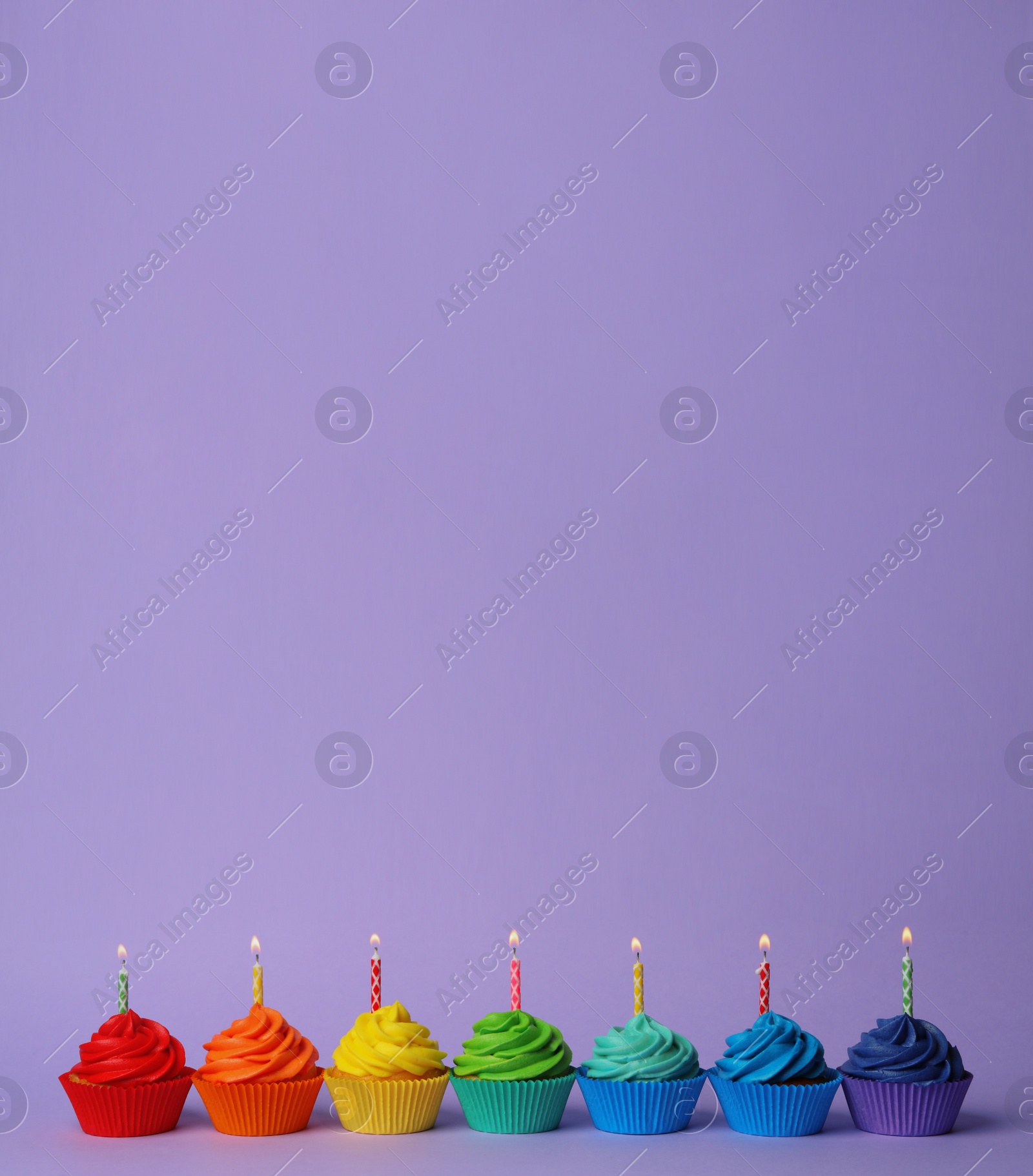 Photo of Delicious birthday cupcakes with burning candles on violet background