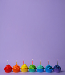 Photo of Delicious birthday cupcakes with burning candles on violet background