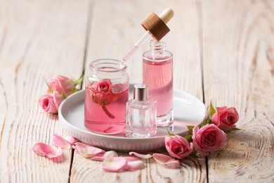 Photo of Bottles of essential rose oil and flowers on white wooden table