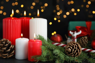 Composition with burning candles on black table against blurred Christmas lights