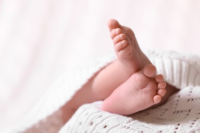 Photo of Cute newborn baby covered in white knitted plaid, closeup of legs. Space for text