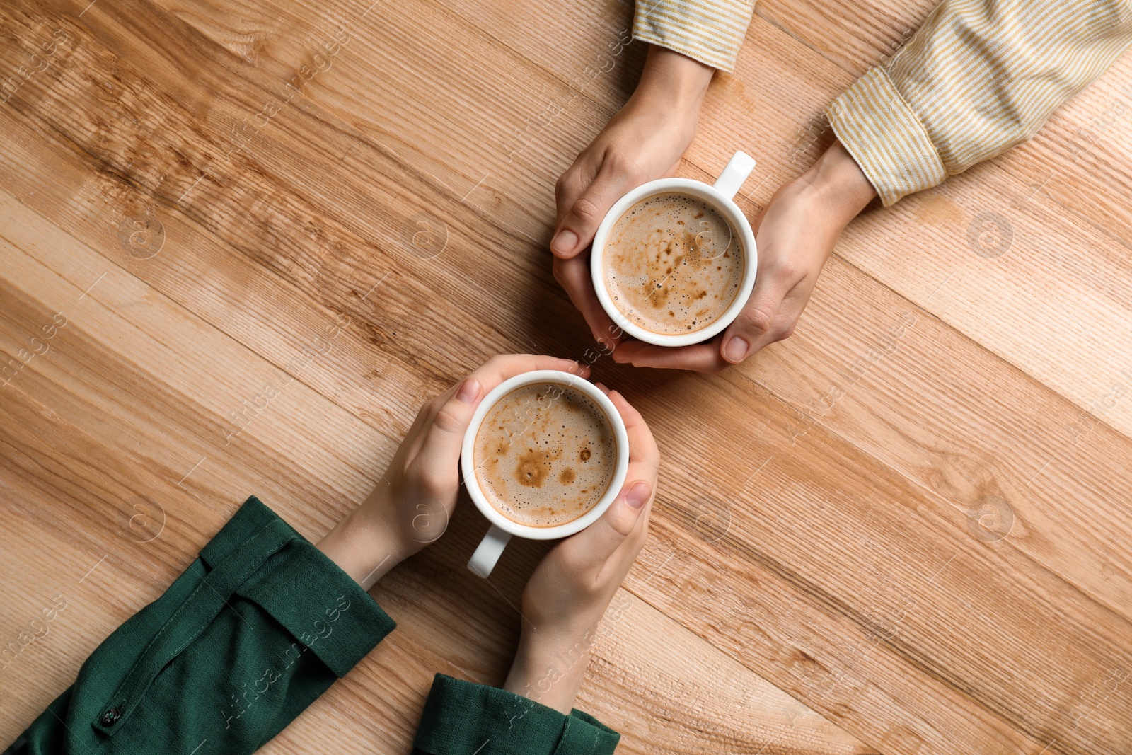 Photo of Women with cups of coffee at wooden table, top view