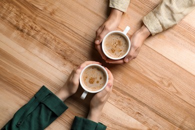 Women with cups of coffee at wooden table, top view