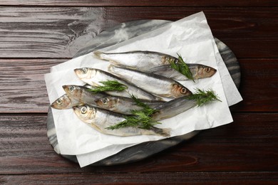 Photo of Fresh raw sprats and dill on wooden table, top view