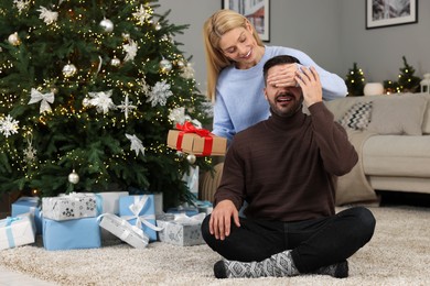 Happy woman surprising her man with Christmas gift at home