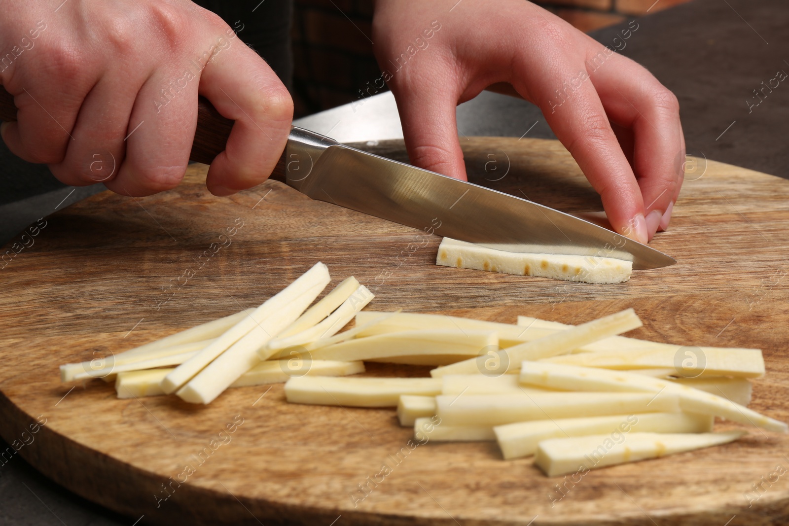 Photo of Woman cutting delicious fresh ripe parsnip at black table, closeup