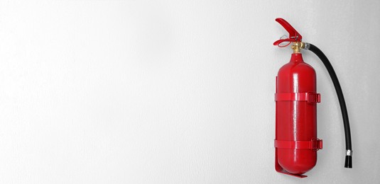 Image of Fire extinguisher hanging on white wall, space for text. Banner design