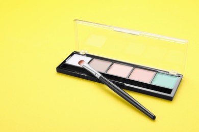 Photo of Colorful contouring palette with brush on yellow background. Professional cosmetic product