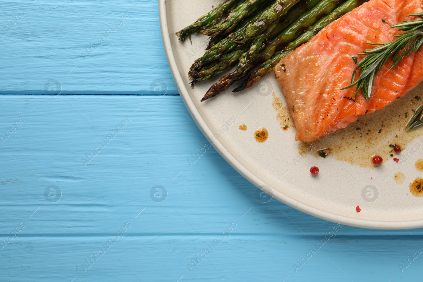Photo of Tasty grilled salmon with asparagus and spices on light blue wooden table, top view. Space for text
