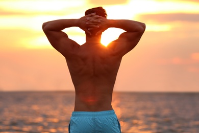 Handsome young man posing on beach near sea at sunset