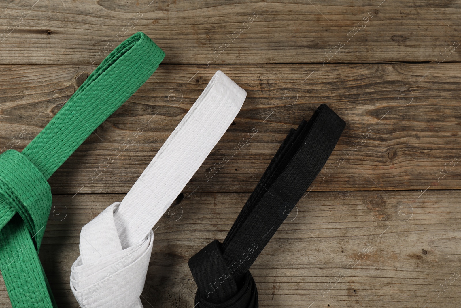 Photo of Colorful karate belts on wooden background, flat lay