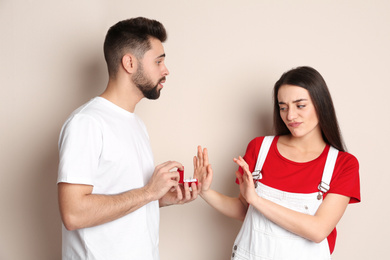 Photo of Young woman rejecting engagement ring from boyfriend on beige background
