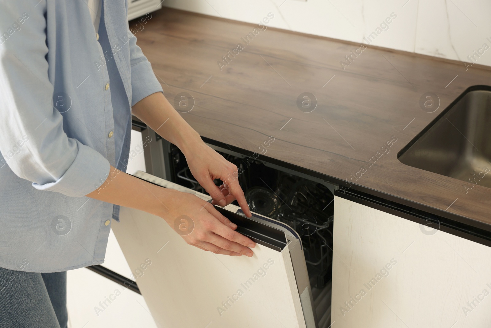 Photo of Woman pushing button on dishwasher's door indoors, closeup