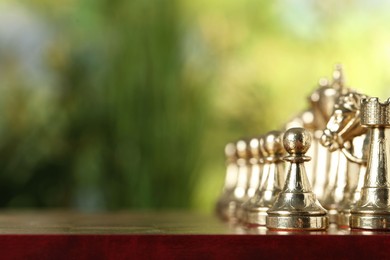 Photo of Golden chess pieces on game board against blurred background, space for text