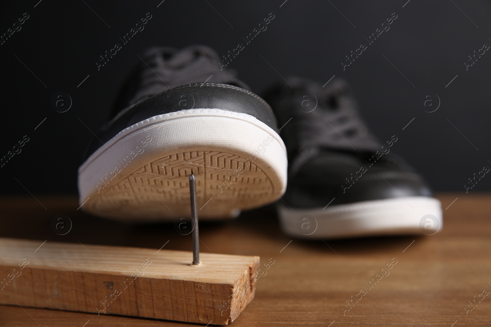 Photo of Metal nail in wooden plank and shoes on table, closeup