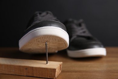 Metal nail in wooden plank and shoes on table, closeup