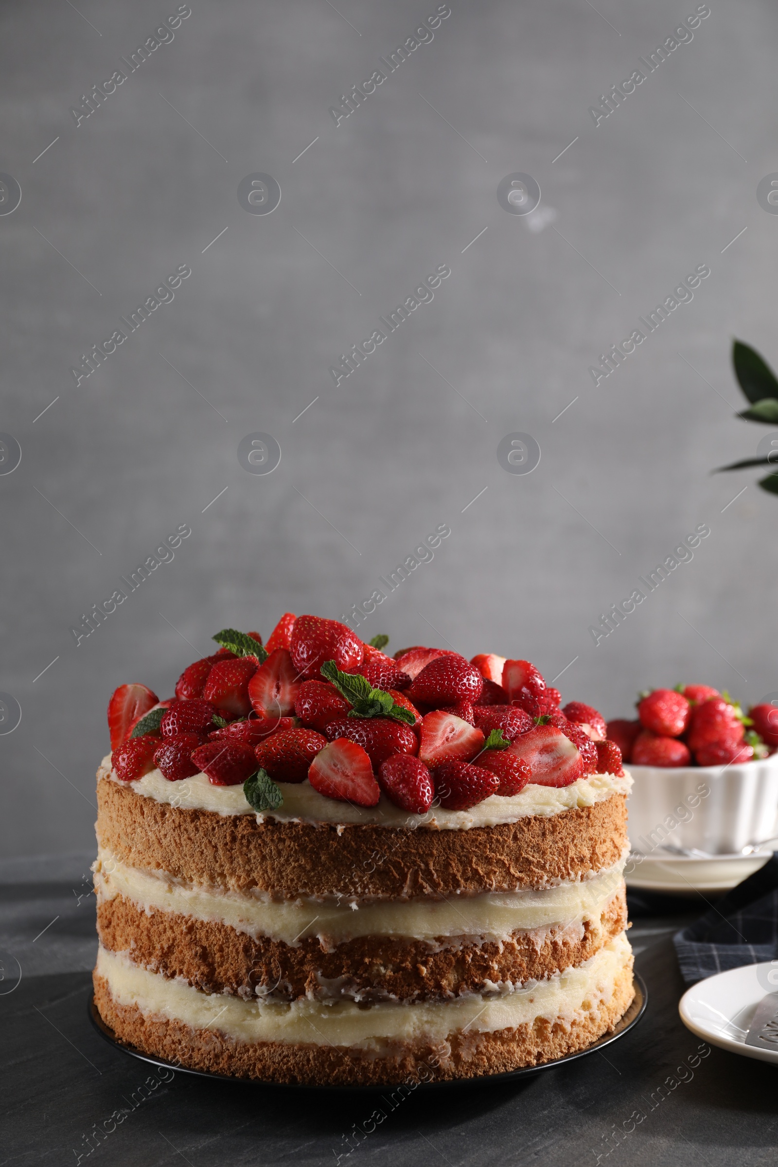 Photo of Tasty cake with fresh strawberries and mint on table against gray background, space for text
