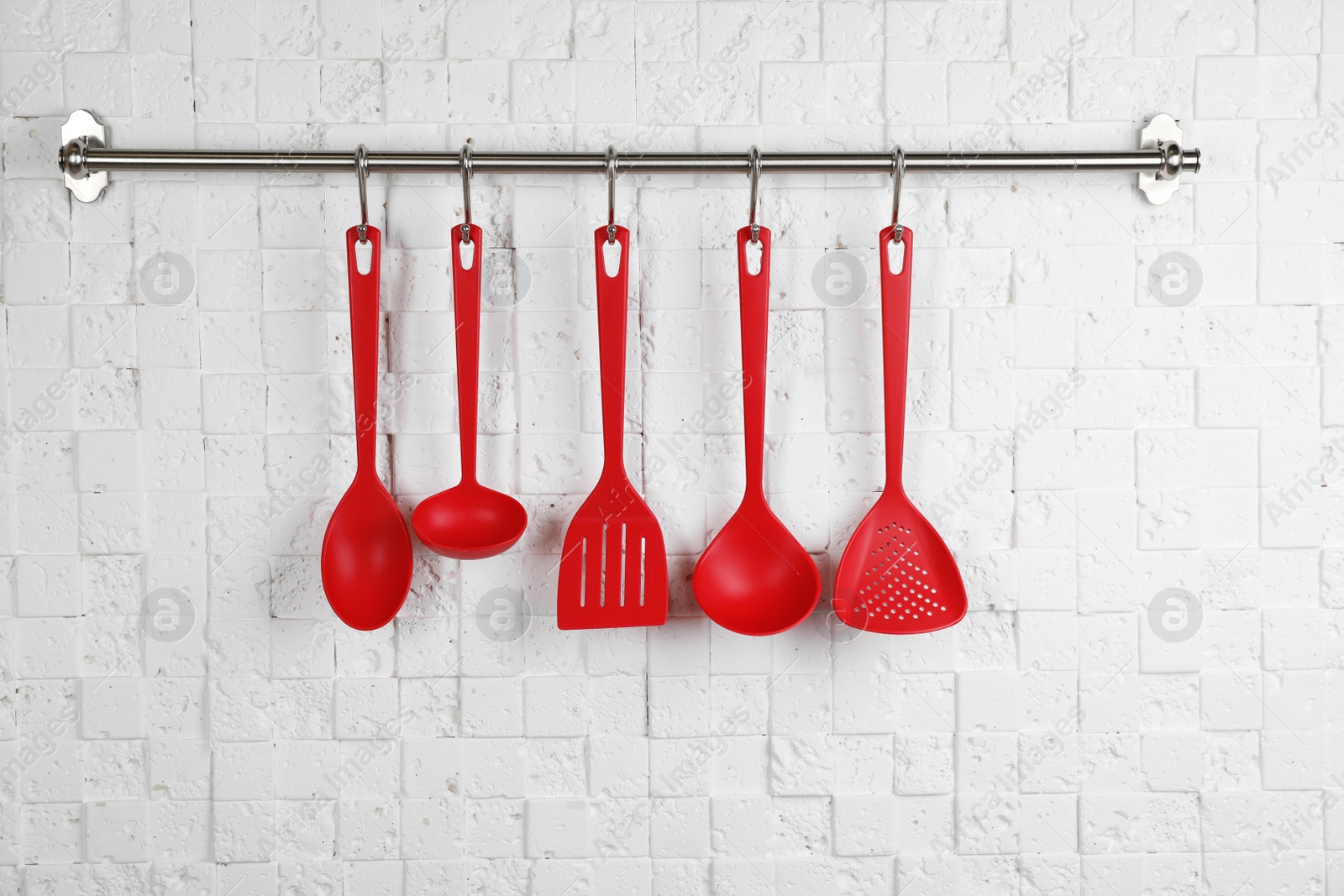 Photo of Rack with clean kitchen utensils on white wall