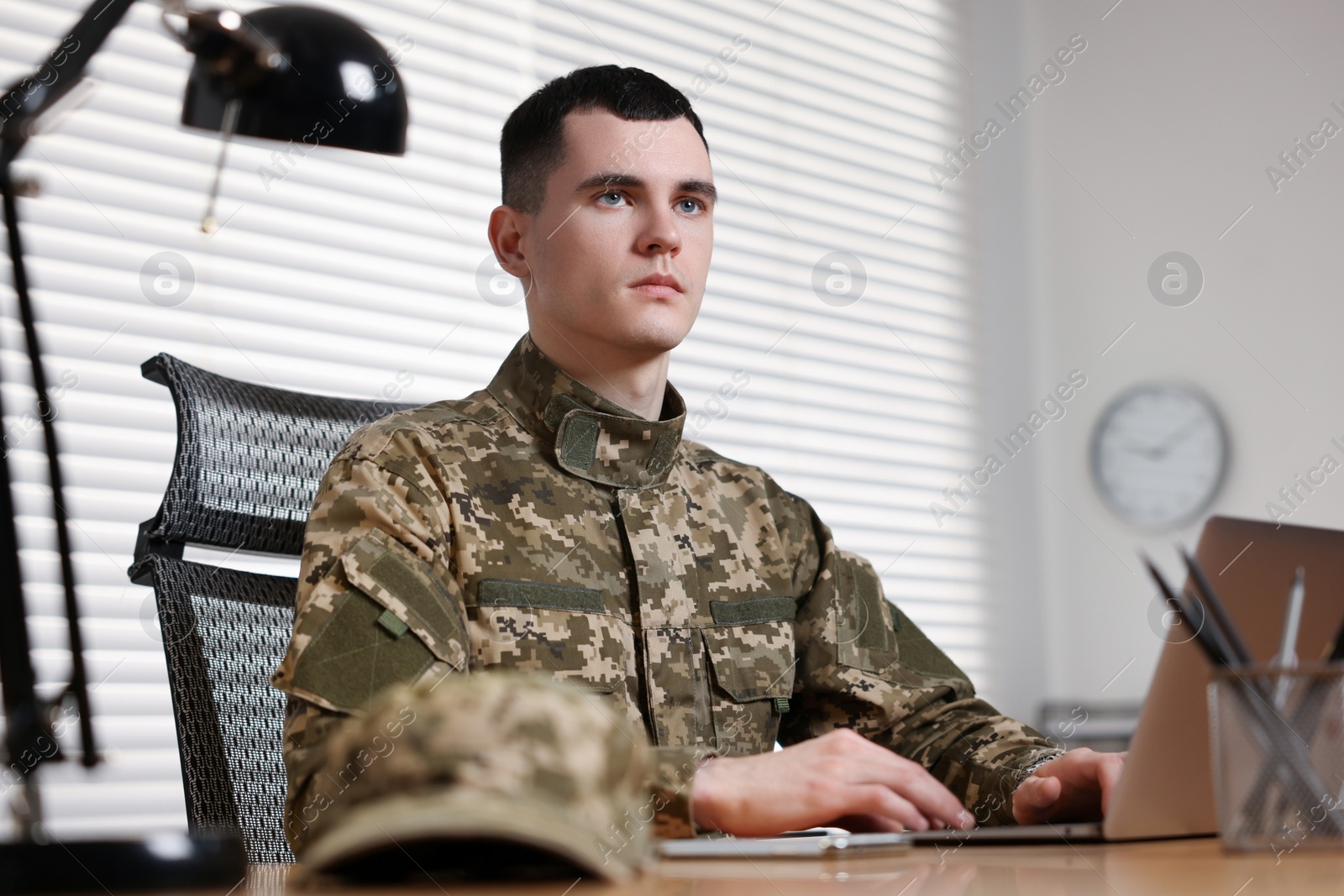 Photo of Military service. Young soldier working with laptop at table in office