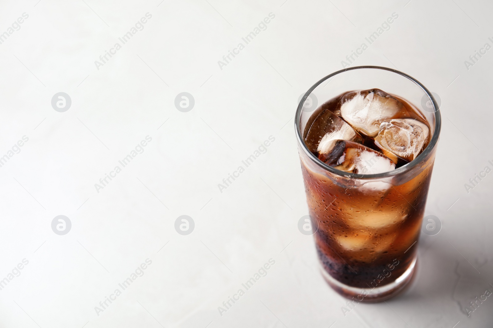 Photo of Glass of refreshing cola with ice on light table. Space for text