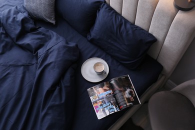 Open magazine and cup of coffee on bed with stylish silky linens in room, above view