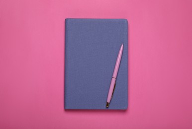 Photo of Blue office notebook and pen on pink background, top view