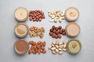 Different types of delicious nut butters and ingredients on grey table, flat lay