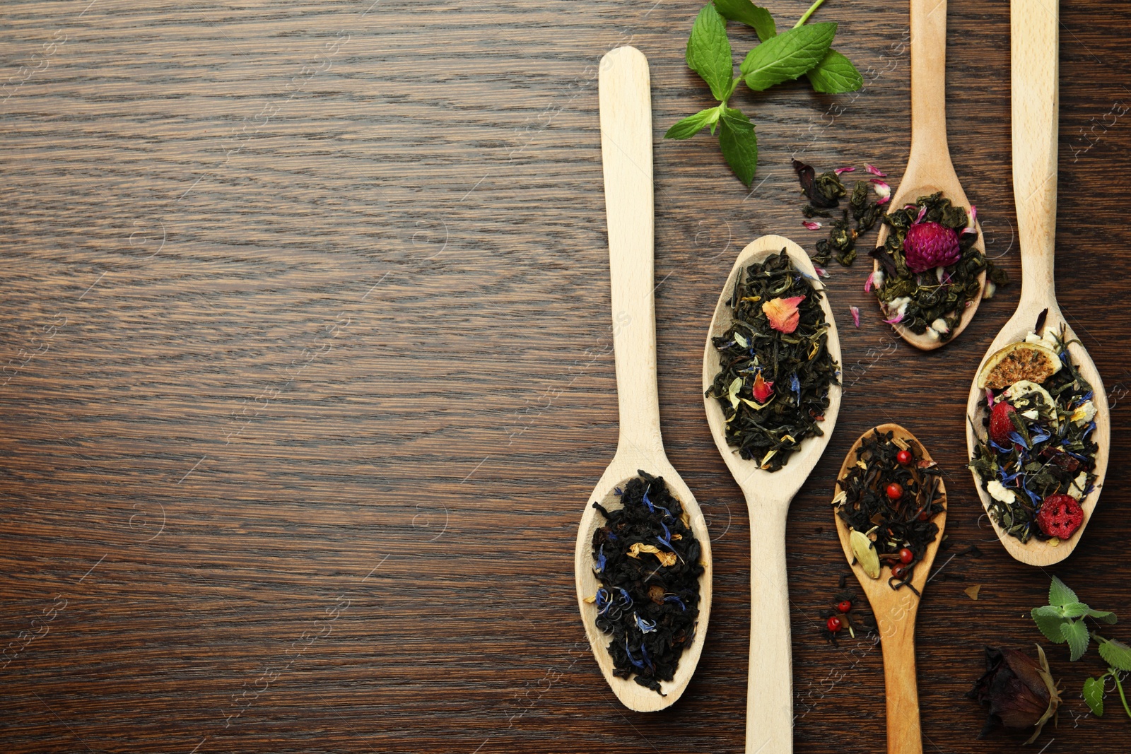 Photo of Flat composition with spoons of dried herbal tea leaves on wooden table. Space for text