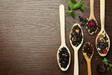 Photo of Flat composition with spoons of dried herbal tea leaves on wooden table. Space for text